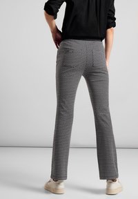 Grå och svarta mönstrade byxor med slim fit, utsvängd nederdel och två bakfickor; kombinerade med ljusa skor i en neutral miljö.