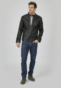 Schwarze Lederjacke mit Reißverschluss, gesteppten Schulterakzenten und Seitentaschen, kombiniert mit blauen Jeans und braunen Stiefeln.