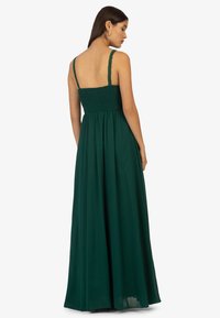 Langes grünes Kleid mit gerafftem Brustteil, dünnen verstellbaren Trägern und fließendem Rock. Es zeichnet sich durch einen leichten Stoff mit einer weichen Textur aus.