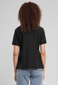 T-shirt nero a maniche corte con vestibilità ampia, realizzato in cotone. Il retro presenta un design semplice, con una texture liscia e senza loghi visibili.