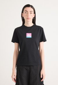 Black t-shirt made of cotton with short sleeves, featuring a colorful cK logo on the chest in pink and blue gradient.
