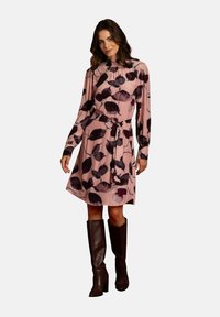 Blumenkleid in Rosa mit langen Ärmeln, gerafftem Ausschnitt, Taillengürtel und dunkelbraunen knielangen Stiefeln. Glattes, leichtes Material.