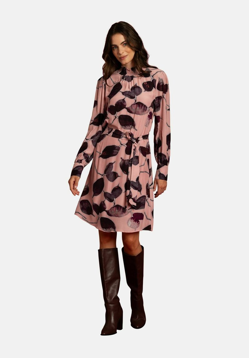 Blumenkleid in Rosa mit langen Ärmeln, gerafftem Ausschnitt, Taillengürtel und dunkelbraunen knielangen Stiefeln. Glattes, leichtes Material.