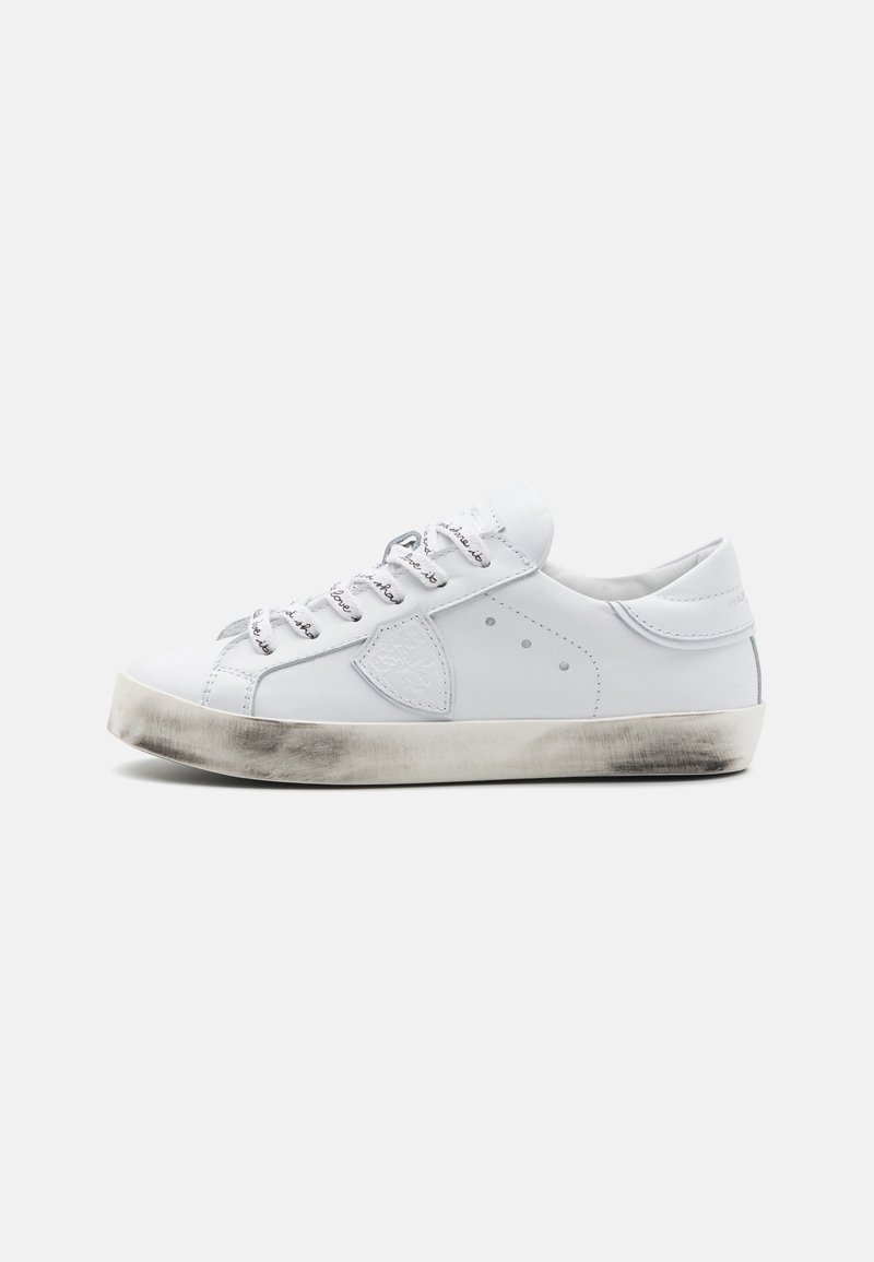 Fehér bőr sneaker, kerek orral, texturált szürke talppal és ezüst fűzőkkel. Jellemzője a logópac és a kis szellőzőnyílások az oldalán.