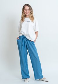 Bílý krátký rukáv tričko s nápisem "COOL MAMA", spárované s volnými světlomodrými kalhotami s elastickým pasem a hladkým povrchem.
