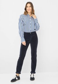 Blauw-wit gestreepte overhemd met lange mouwen, gecombineerd met donkerblauwe corduroy broek en zwarte sneakers met witte accenten.