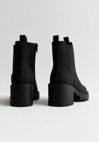 Svarta ankelskor med en tjock hög klack, slät matt yta, dragkedjestängning på sidan och dragflikar bak för enkel påtagning.