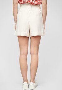 Kremfargede, knelengde shorts med bred kant, elastisk midje og detaljert søm. Båret med hvite joggesko.