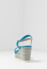 Základové sandály v tyrkysovém semiši s nastavitelným nártem a proužkovanou tkanou platformou. Hladký povrch s zaobleným podpatkem.