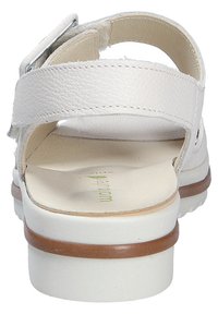 White leather sandal with an ankle strap, open back, white sole, and light brown wooden heel detailing. Soft inner lining visible.