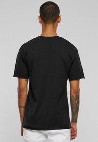 Černé bavlněné tričko s krátkými rukávy, kulatým výstřihem a uvolněným střihem. Má hladkou texturu a minimalistický design.