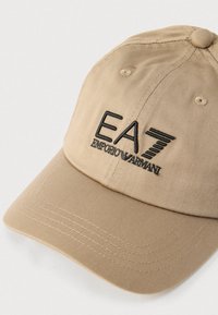 Șapcă de baseball din bumbac bej, cu vizieră curbată, având logo-ul „EA7” brodat negru și textul „EMPORIO ARMANI” pe partea din față.