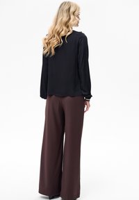 Czarna bluzka z długim rękawem o luźnym kroju, zestawiona z wysokim stanem, szerokimi brązowymi spodniami, oba wykonane z gładkiej, lekkiej tkaniny.