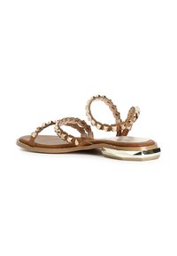 Tan väriset litteät sandaalit, joissa on kaksi ümmargust rihma, metallistudid, tekstuurne sisetust ja kuldsete aktsentidega geomeetriline kontbase.