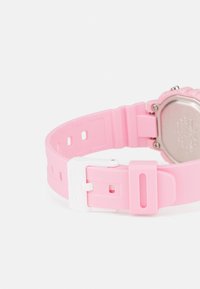 Bracelet de montre en silicone rose avec une boucle blanche. Présente un design texturé et des trous ajustables pour un meilleur ajustement. Boîtier en métal visible au dos.