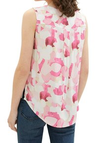 Blouse sans manches blanche, ornée d'un motif abstrait rose. Tissu doux avec un ourlet arrondi et un détail de pli au dos.