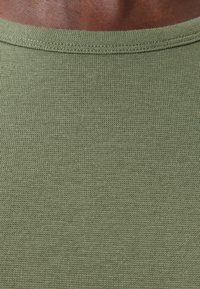 Tela de punto verde oliva con una textura acanalada. El escote es de forma redonda clásica, con detalles de costura visibles.
