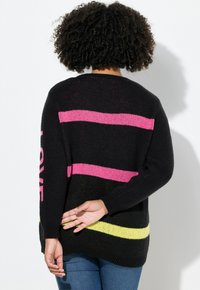 Svart stickad tröja med horisontella ränder i rosa och gult, med "LOVE"-text på ärmen. Mjuk textur, avslappnad passform.