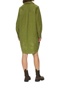 Vestido de camisa de pana verde con mangas largas, detalle de pliegue en la parte posterior y dobladillo asimétrico. Combinado con botines marrones.