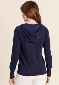 Marineblaue Kapuzenjacke mit lockerem Schnitt, weicher Strickoberfläche, verstellbarem Kapuzenzug und gerippten Bündchen und Saum. Einfaches Design ohne Verzierungen.