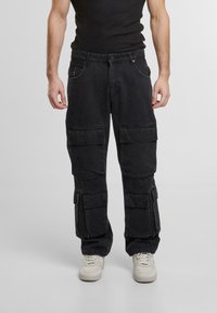Pantaloni de tip cargo negri, cu multiple buzunare mari, confecționați dintr-un material durabil. Talie ajustată și design cu picior drept, asortați cu adidași albi.