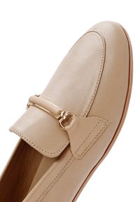 Mocassini in pelle beige con una fascia e dettagli metallici dorati, caratterizzati da una punta arrotondata e sottili dettagli di cucitura.