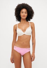 Brassiere color crema con merletti e spalline regolabili, abbinato a mutandine rosa con dettagli in pizzo e un piccolo fiocco in vita.