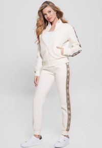 Cream zip-up sweatshirt and matching joggers with a side stripe pattern, made of soft fabric. Features pockets and ribbed cuffs.