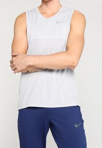 Canotta atletica grigia chiara con scollo tondo e design testurizzato; presenta un piccolo logo Nike grigio. Abbinata a pantaloni corti blu navy.
