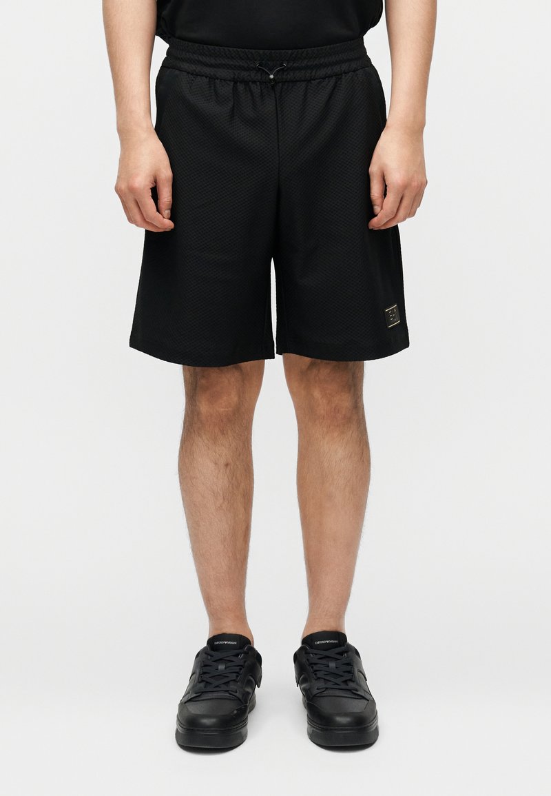 Μαύρο δίχτυ σορτς με ελαστική μέση, μήκος μέχρι τη μέση του μηρού, με διακριτικό υφασμάτινο μοτίβο και μικρό λογότυπο ως διακοσμητικό στοιχείο.