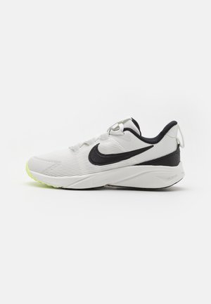 Zapatilla deportiva blanca con parte superior texturizada, acentos en negro, sistema de cordones seguro y suela en verde neón. Presenta elementos de diseño similares en ambos lados.