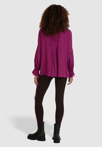 Violetti pitkähihainen paita, jossa on laskostettu selkä, yhdistetty mustiinlegginsseihin, joissa on vaaleanpunainen sivu-urheilusi ja mustat nilkkasaappaat.