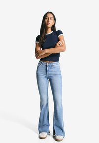 Marineblå kortærmet top med hvid kant, parret med blå flagrende jeans. Bemærkelsesværdige detaljer inkluderer højt talje og splitkanter. Casual fodtøj.