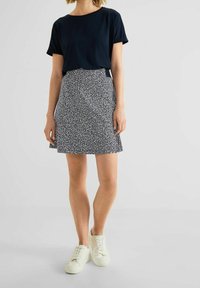 Námornická posádka tričko s kulatým výstřihem v námořnické modři v kombinaci s sukní po kolena s černobílým vzorem. Bílé tenisky dotvářejí celkový vzhled. Hladká textura látky.