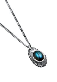Zilveren ketting met een geslagen hanger waarop een ovale labradorietsteen schittert in blauwe en groene iridescentie. De ketting heeft een rond schakeldesign.