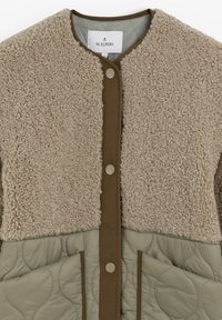 Chaqueta acolchada beige y verde oliva con parte superior de sherpa, botones a presión en el frente y dos bolsillos delanteros.
