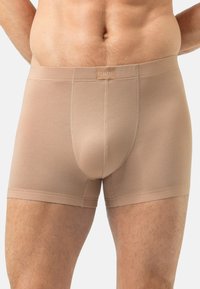 Beżowe bokserki o fakturowanej strukturze, noszone przez stojącego mężczyznę, pokazane od talii do połowy uda na białym tle.