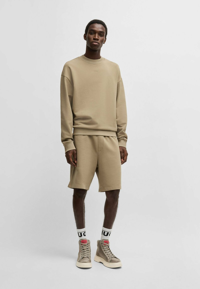 Beige bomulds-sweatshirt med dropped shoulders, parret med matchende shorts. Har crew neckline og ribbede manchetter; iført beige høj-top støvler.