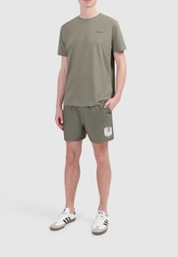 Olijfgroene katoenen t-shirt met een ronde halslijn en logo, gecombineerd met bijpassende shorts met zijzakken en witte tekstdetails.
