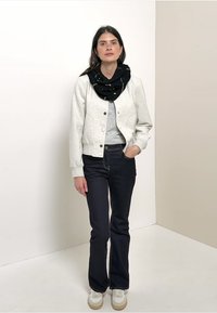 Light grey bomber jacket with snap buttons, worn over a grey top. Dark jeans and a black patterned scarf. White sneakers with beige soles.