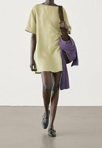Robe courte jusqu'aux genoux, manches courtes, en lin jaune clair, associée à une écharpe tricotée violette et un sac en cuir marron. Chaussures plates noires avec boucle.