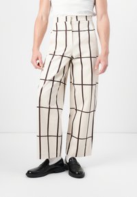 Pantaloni a gamba larga crema con un audace motivo a quadri marroni, realizzati in tessuto morbido con un design a vita alta su misura. Scarpe nere completano il look.