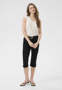 Top bianco senza maniche con piccoli pois neri, dettaglio arricciato sulle spalle, abbinato a pantaloni cropped neri a vita alta e sandali neri.