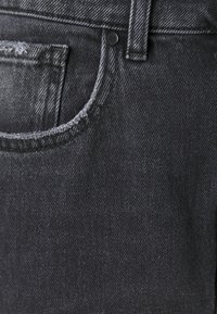 Black denim jeans featuring a subtle texture, top-stitching along the pocket, and a black button at the waist.