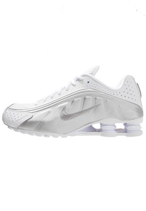 Chaussure de course blanche Nike avec un swoosh argenté, des trous de ventilation latéraux et des ressorts amortisseurs visibles sous la semelle.