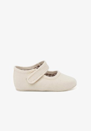 Chaussure en toile beige clair avec un bout arrondi et deux bandes Velcro, présentant une doublure intérieure à carreaux et une surface texturée.