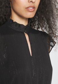 Μαύρο φόρεμα με ρυτιδωτό γιακά και άνοιγμα τύπου κλειδώματος. Φτιαγμένο από υφασμάτινη υφή με κατακόρυφες ρίγες και διαφανή κοντά μανίκια.