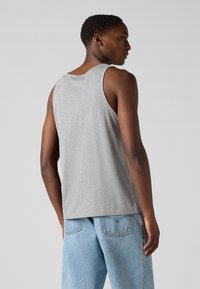 Débardeur sans manches gris en tissu doux avec une coupe décontractée, associé à un jean en denim bleu clair à coupe classique et avec deux poches arrière.