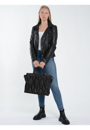Sort quilteret håndtaske med en struktureret form, dobbelte top-håndtag og lynlås lukning. Båret af en person i en sort læderjakke og jeans.