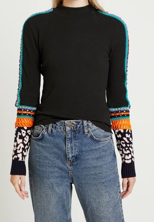 Top nero a maniche lunghe con motivi a maglia colorati sulle maniche, abbinato a jeans di denim blu a vita alta.